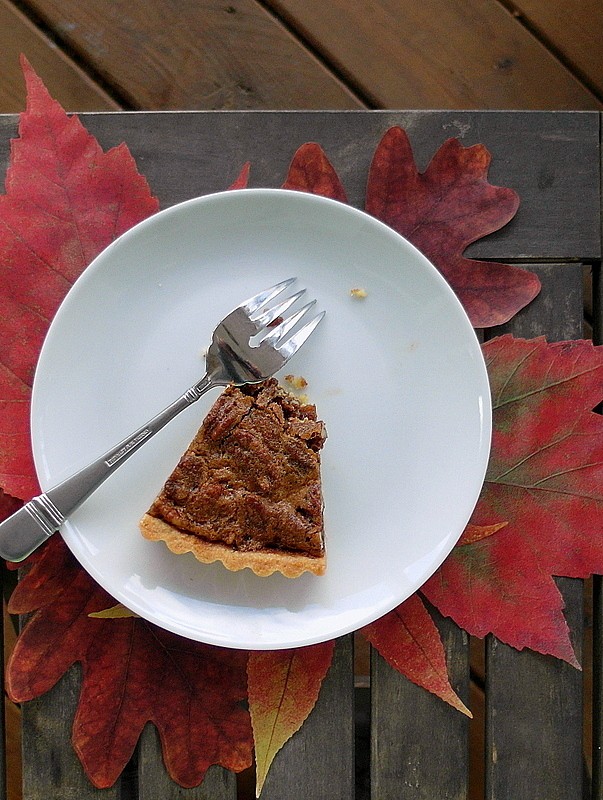 A slice of coffee pecan tart on a plate with fall leaves under it.