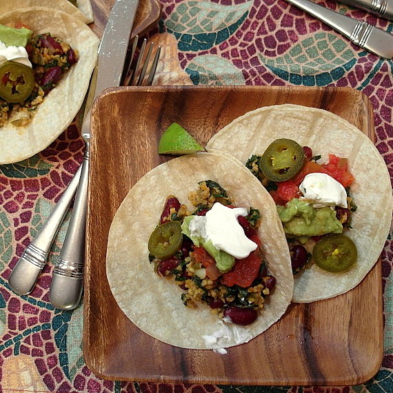Veggie Oat taco mince on two corn tortillas with jalapenos, guacamole, and sour cream garnish. They are plated on wooden plates and there is a wedge of lime garnish. 