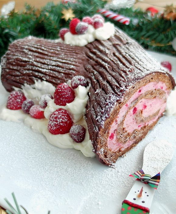Chocolate buche de noel yule log with whipped cream and berries.