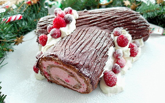 chocolate buche de noel on a white platter decorated with whipped cream and berries