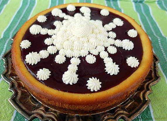 A whole orange ricotta mascarpone cheesecake with cranberry puree. Served on a silver platter.