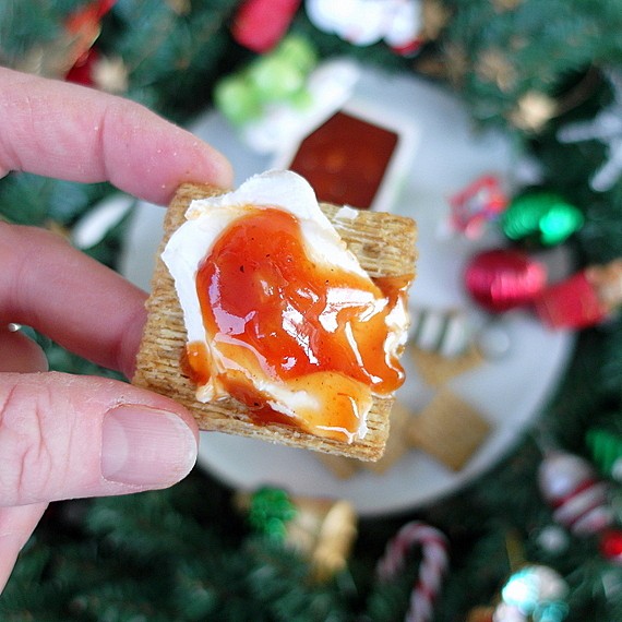 cream cheese and red sauce on a woven wheat cracker over a plate with Christmas decorations.