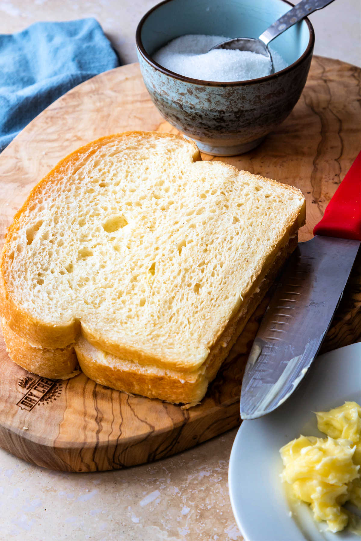 A sandwich made on white bread on a small cutting board with sugar in a small bowl in the background.