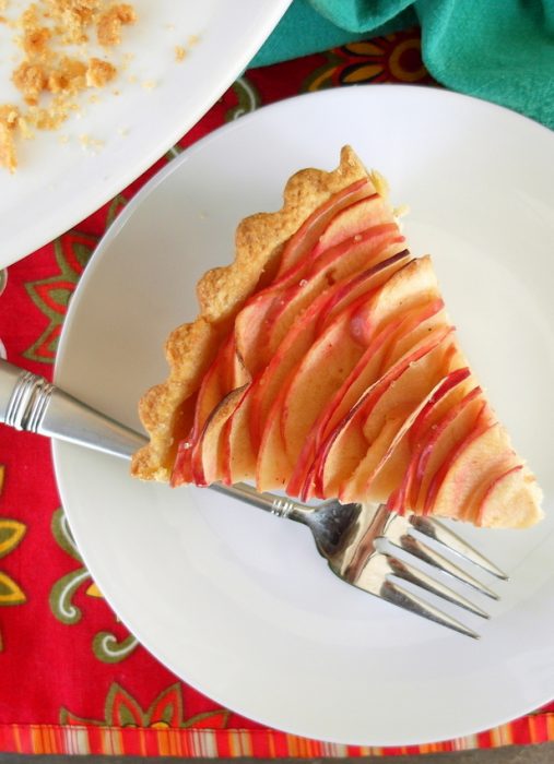 A slice of chai apple cheesecake tart with a fork on a white plate.