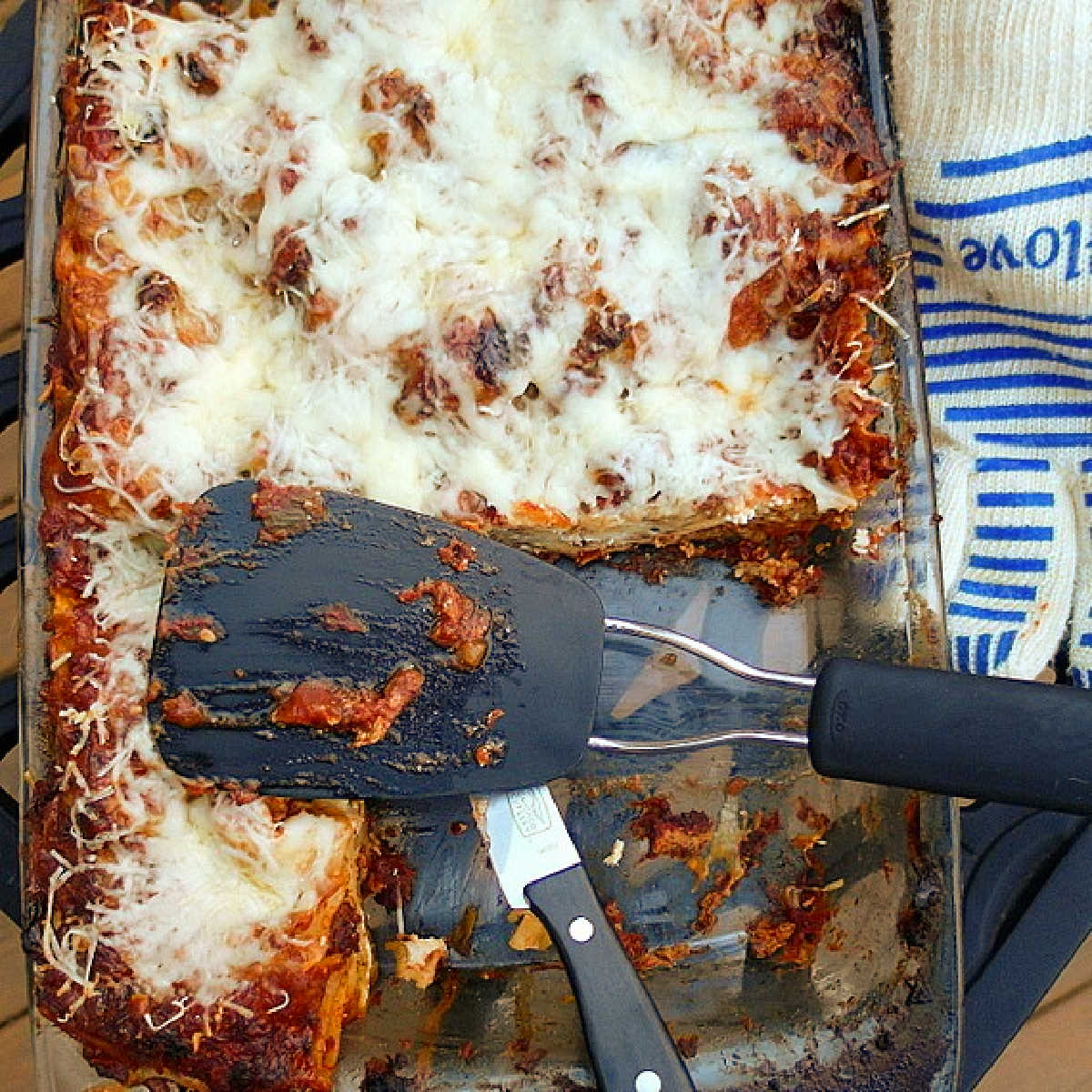An overhead shot of a glass pan of lasagna with a couple of pieces cut out of it and a black spatula.