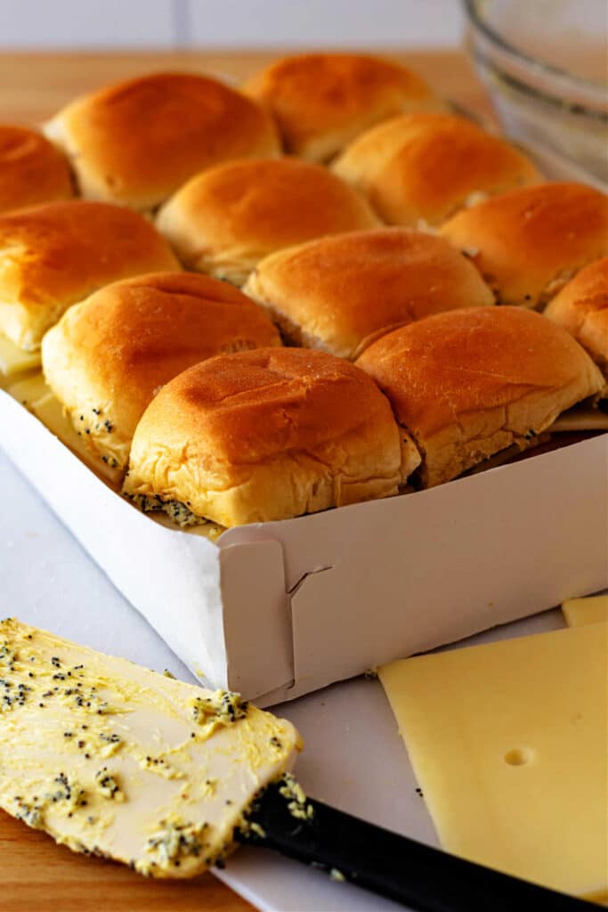 A white paper tray of 12 slider buns filled with poppy seed and butter filling, ham, and cheese.