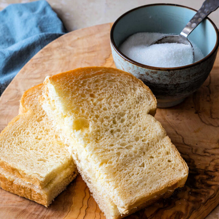 A sandwich made on soft white bread cut in half with one half resting on the other and a bowl of granulated sugar.