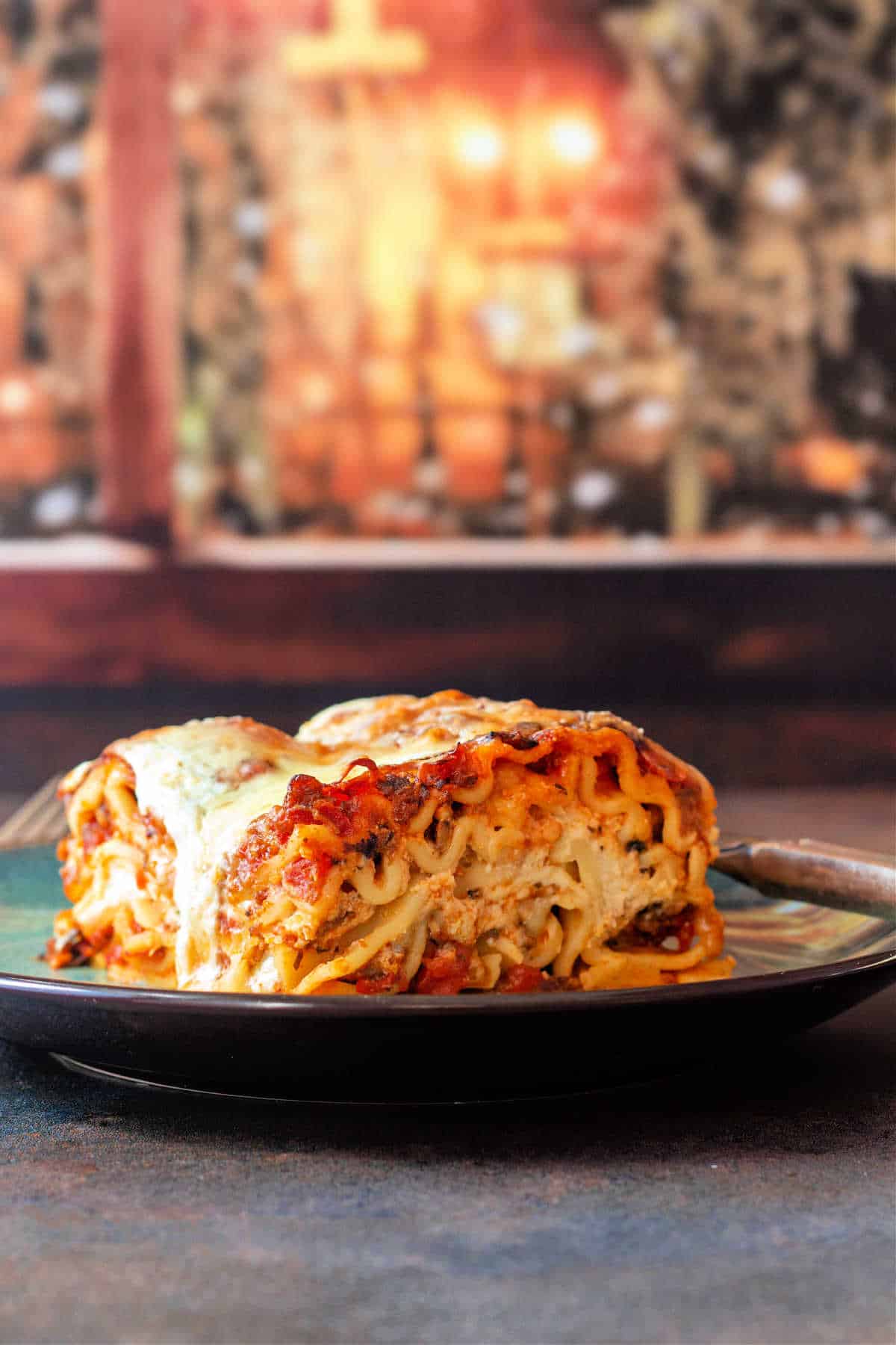 A large square of Italian sausage lasagna on a plate in front of a window at night.