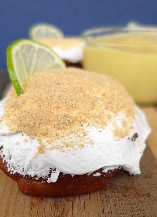 Single key lime pie doughnuts with key lime curd in background. A slice of lime for garnish.