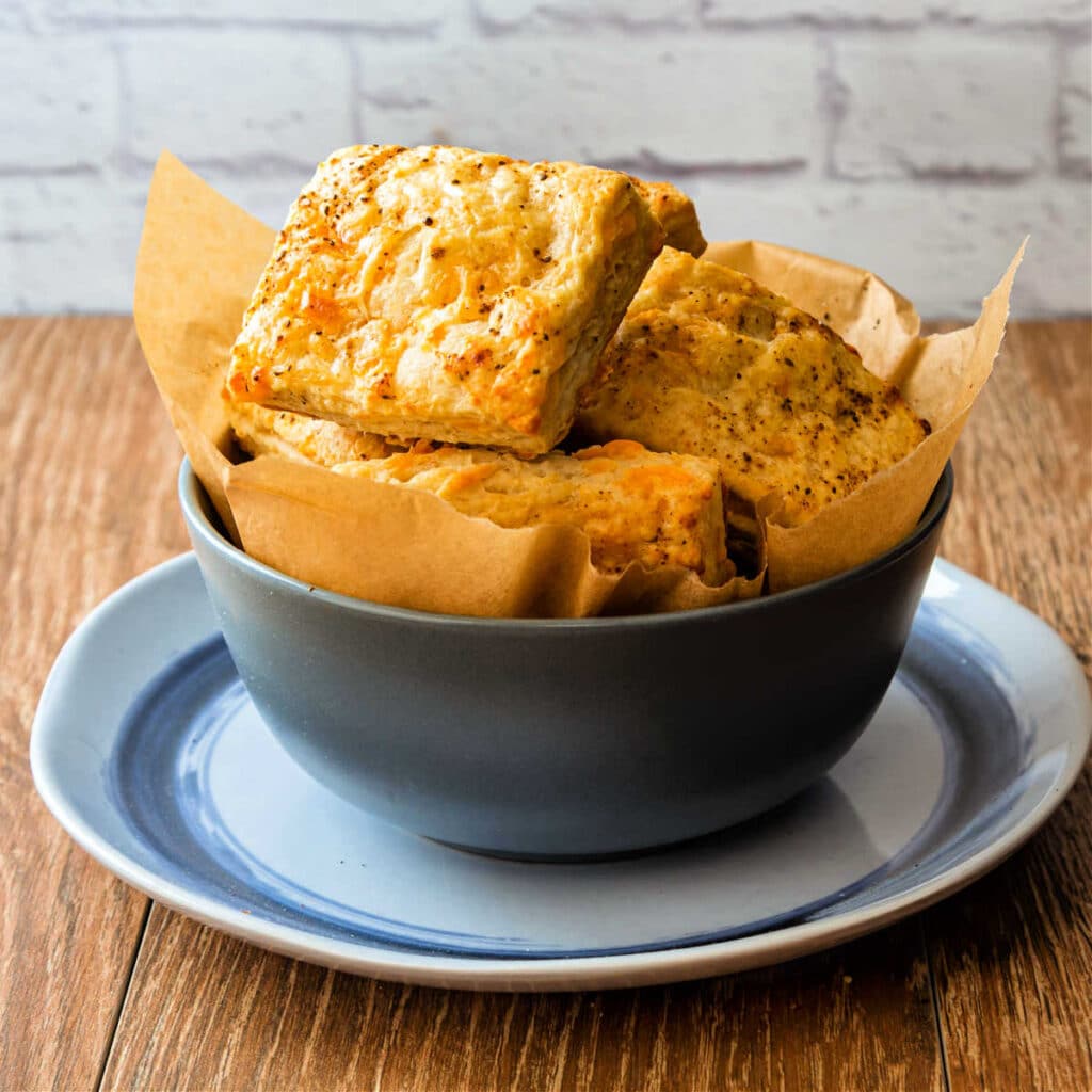 A gray bowl filled with flaky cheddar biscuits sitting on a light blue plate.
