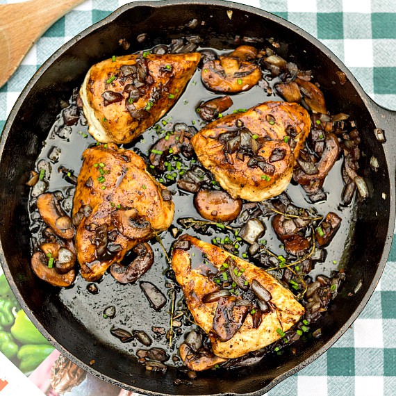 Overhead shot of black cast iron pan with cooked chicken thighs, mushrooms, and thyme.