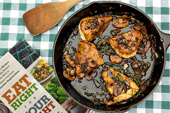 Overhead shot of the Eat Right for Your Sight cookbook and a cast iron skillet with 4 chicken thighs.