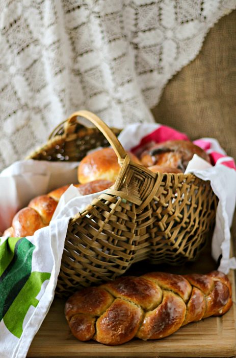 A basket of braided bread loaves with a braided loaf in front of it.
