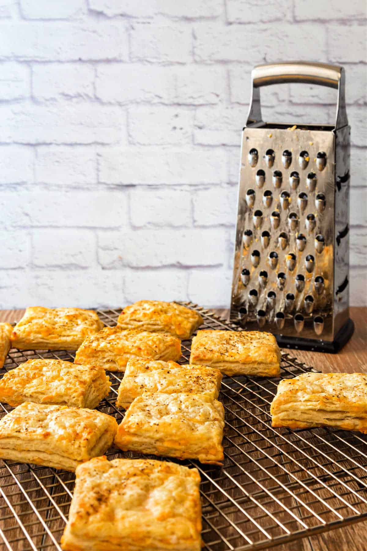 A cooling rack with square biscuits and a cheese grater in the background.