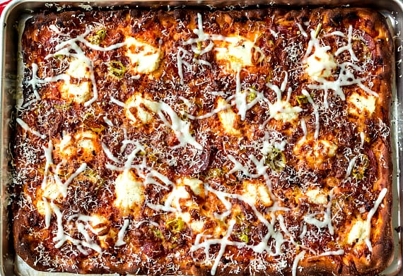 An overhead shot of a large rectangular grandma pizza cooked on a baking sheet.