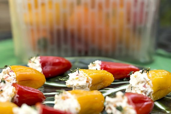 Red, yellow, and orange mini peppers stuffed with agoat cheese filling on a green plate.