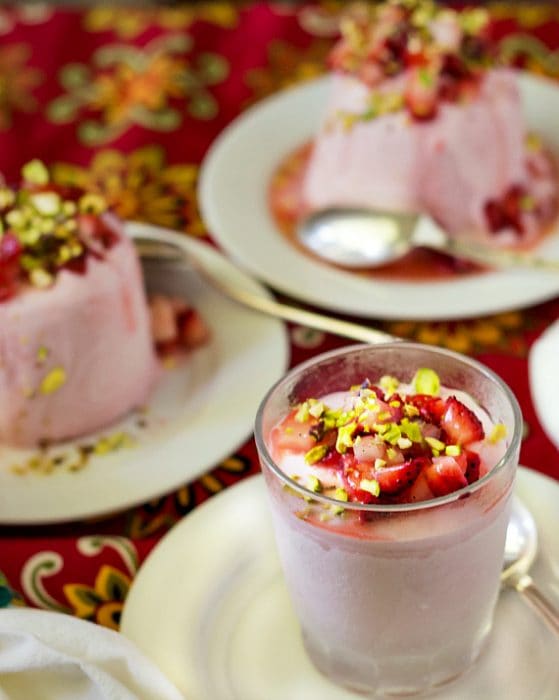 Close up image of strawberry kufli served in a clear glass, topped with diced strawberries and chopped pistachio nuts.
