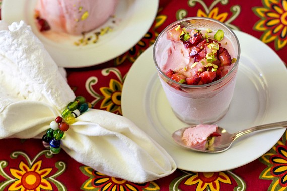 A  strawberry rose kulfi with pistachios and diced strawberries, with one bite taken out on a silver spoon.