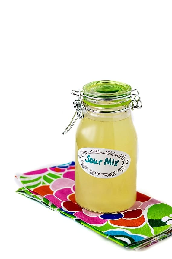 A sealable bottle of homemade sour mix on a floral napkin. Label on the bottle reads "Sour Mix".