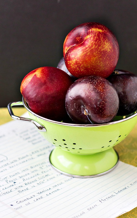 Gorgeous red and black plums, in a green colander with a handwritten recipe for German plum cake