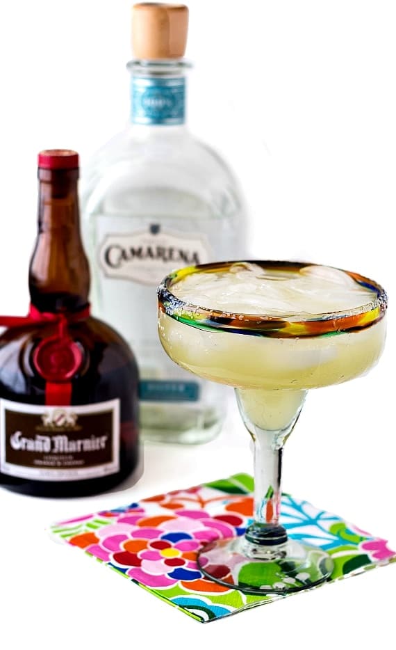 A full margarita glass on a floral napkin with a bottle of Grand Marnier and one of Camarena tequila in the background.