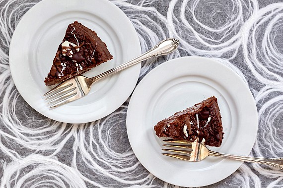 Overhead shot of two slices of chocolate cheesecake on white plates with forks ready for serving.