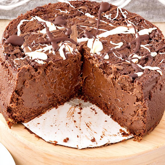 A chocolate cheesecake with a large wedge cut out of it, showing dense chocolatey interior. Cheesecake is sitting on a cardboard cake circle.