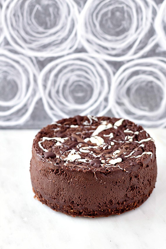 Whole 6 inch chocolate cheesecake splattered with dark, white, and milk chocolate across the top. 