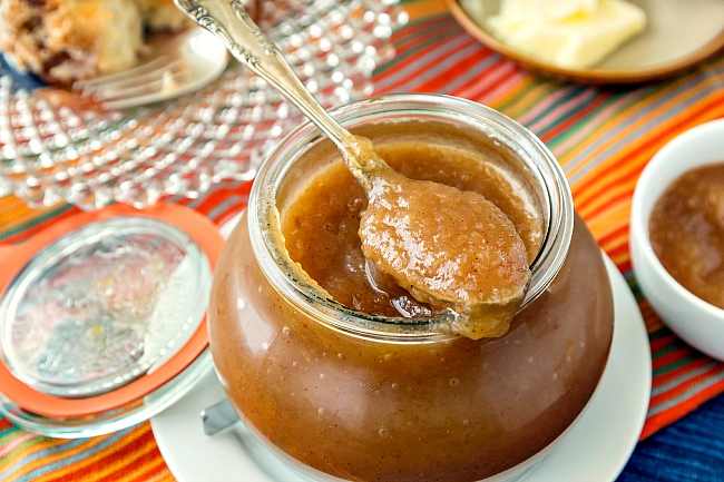 A glass jar of Chai Spice Apple Butter with a silver spoon.