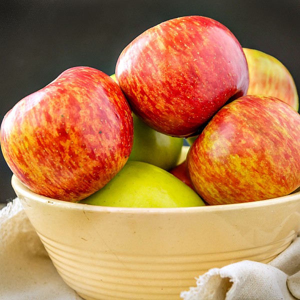 A yellow pottery bowl filled with fresh apples.