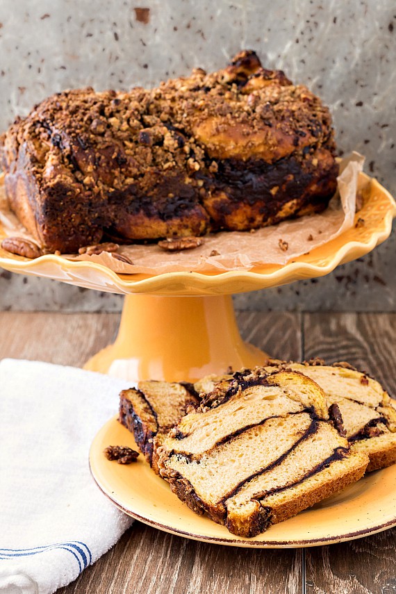 An orange cake stand with a loaf of babka and an orange plate with 3 slices of pumpkin babka on it.