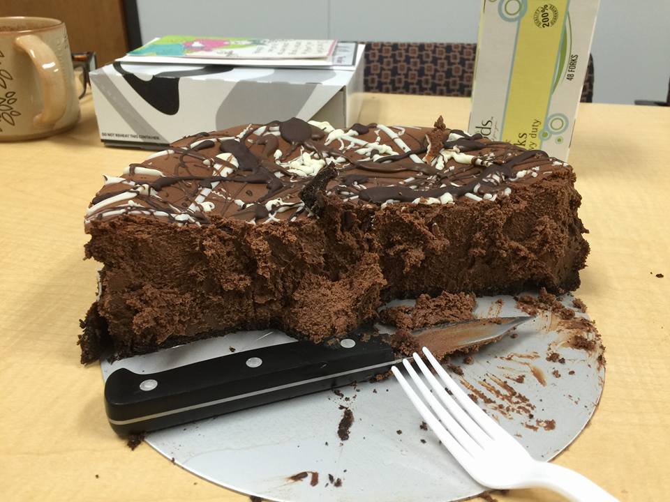 Half of a chocolate cheeseckae inexpertly cut on a cake circle with a knife and a plastic fork.