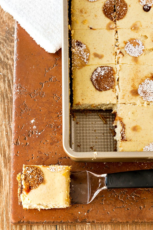 A pan of cheesecake bars cut into squares with one removed.