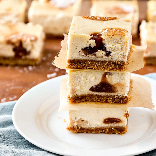 Maple Apple Butter Polka Dot Cheesecake Bars stacked up with parchment paper between each slice on a white plate.
