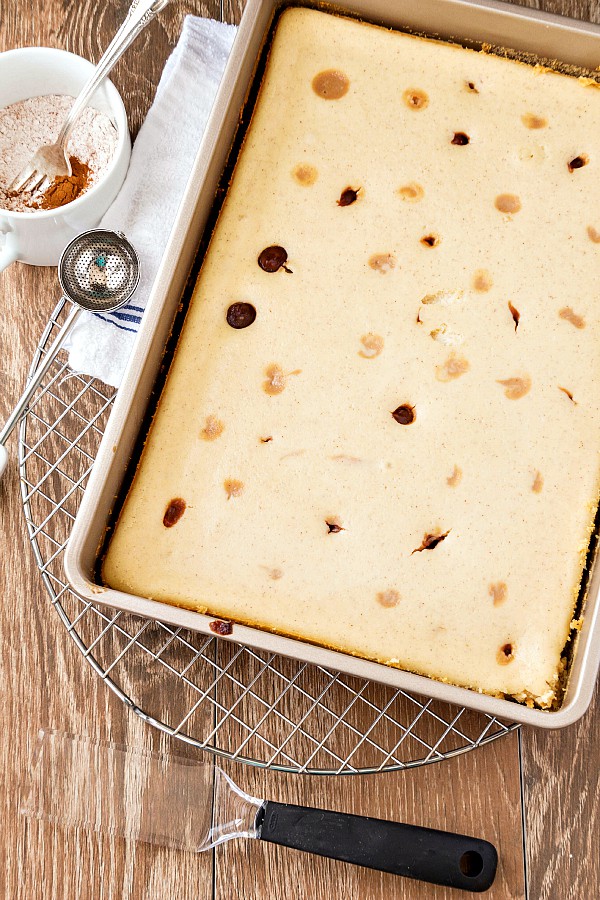 Pan of baked cheesecake bars, cooling on a rack.