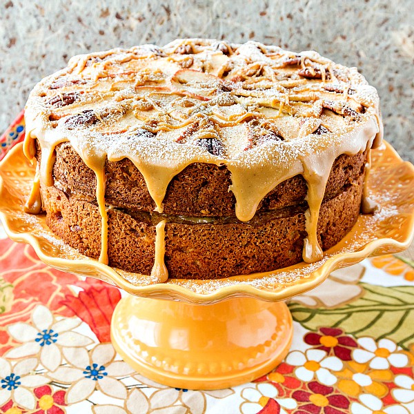 A whole spiced apple cake on an orange cake stand, with a light sprinkling of confectioners sugar over all.