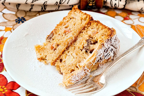 A slice of spiced apple cake on a white plate with a silver fork.