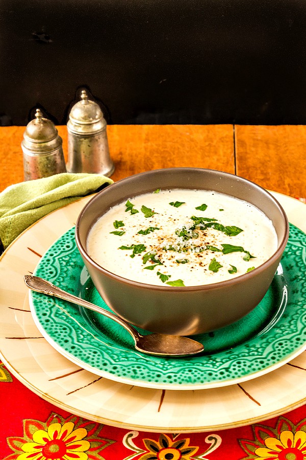 A brown bowl of cream of cauliflower soup on a green plate.