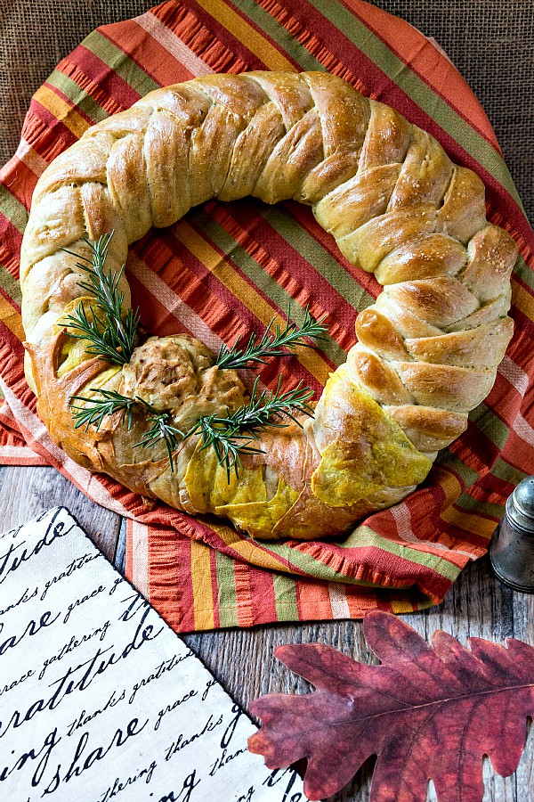 A braided bread wreath decorated with rosemary on a striped napkin,