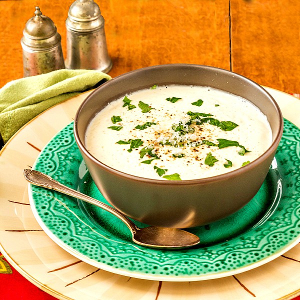 A bowl of cream of cauliflower soup on a green plate with chopped herbs for garnish.