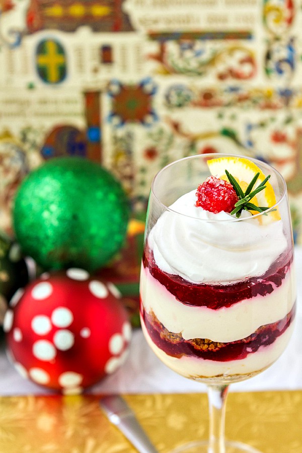 A wine glass of dessert topped with whipped cream, a sugared cranberry, and a small sprig of rosemary.