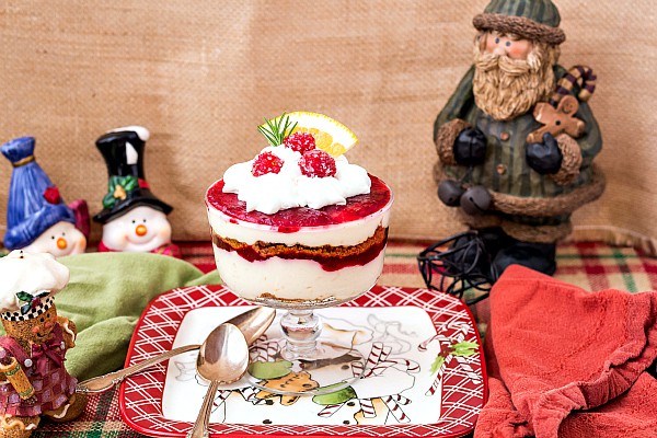 An individual trifle dish with cheesecake parfait on a table with holiday decorations.