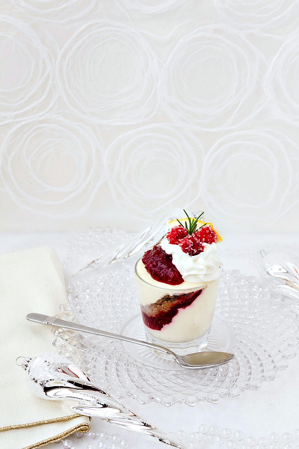 One no-bake orange cranberry cheesecake parfaits ready to serve on a clear glass plate with silver spoon.