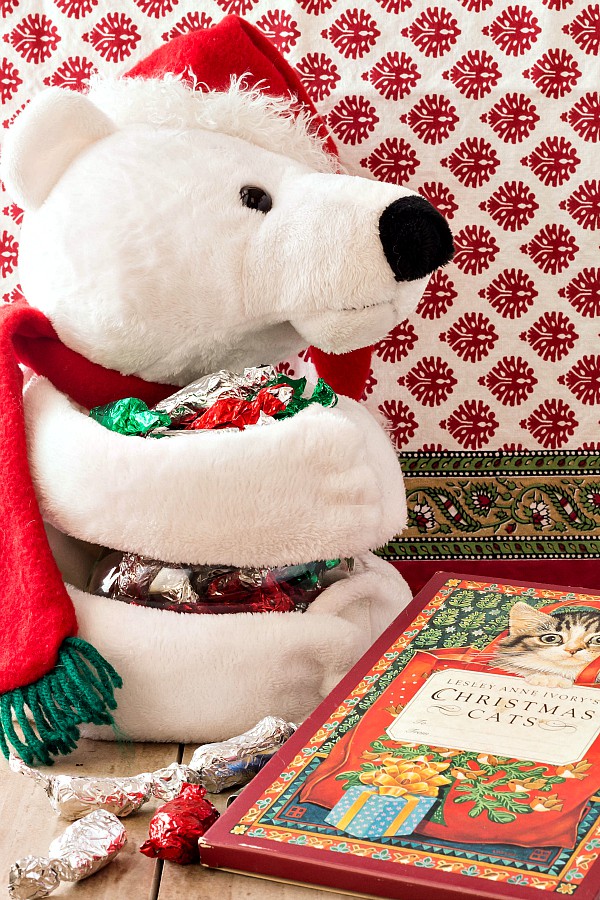 A white stuffed bear with red hat holding wrapped candies.