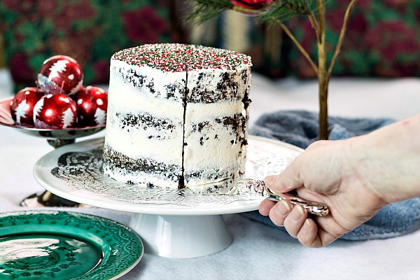 A hand with knife slicing a 3-layer chocolate cake with white icing.