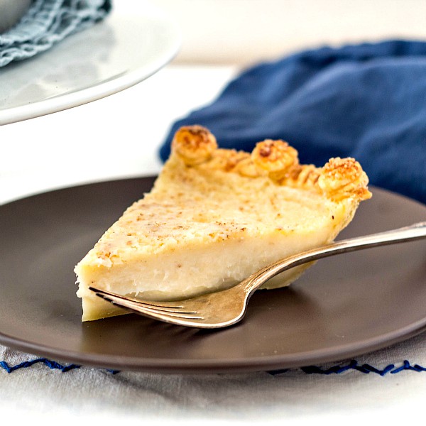 A slice of sugar cream pie on a brown plate with a silver fork ready for serving.