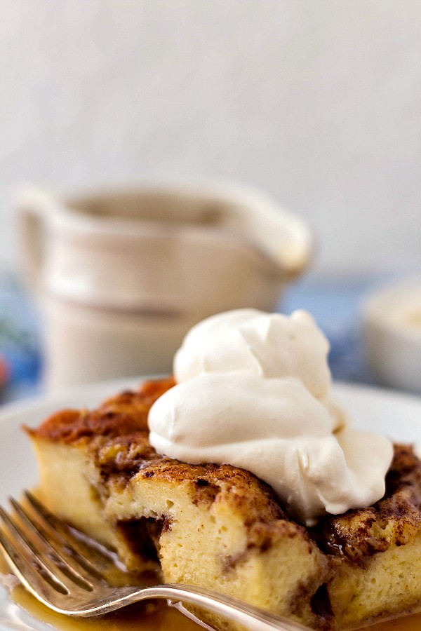 Close up of Moravian sugar cake bread pudding on a plate with syrup and whipped cream.