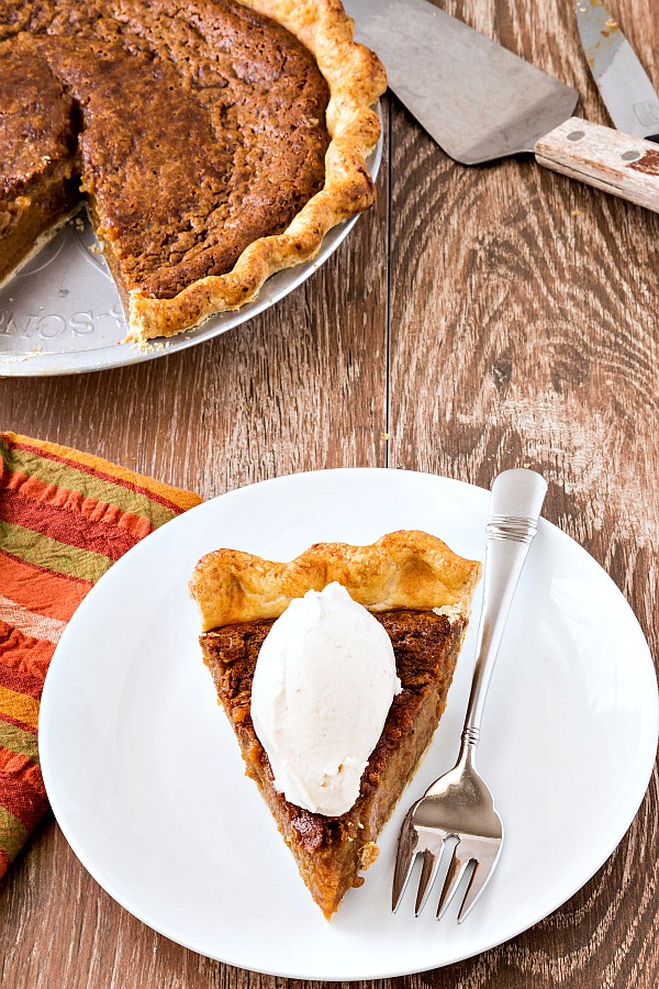 A piece of sorghum pie on a white plate with a fork and a quenelle of ice cream on top.