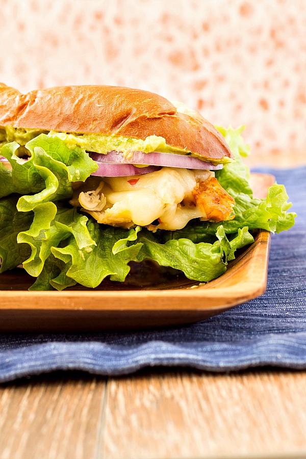A large sandwich on a plate with a lot of lettuce, cheese, and chicken.