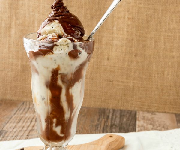 hot chocolate sauce pouring over a sundae glass of ice cream
